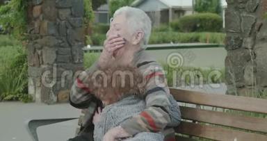 当一个年轻的男孩坐在公园的长凳上拥抱时，一个年长的女人拥抱和挤压，男孩说了一些有趣的话，她笑了起来
